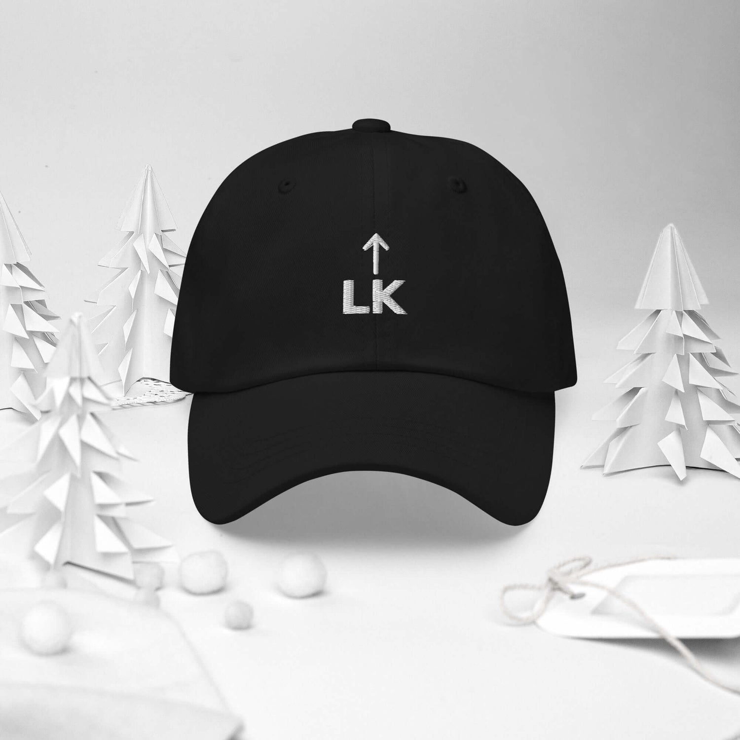 corner cap jnjdjdnbjnddbnksckn black cap with LK embroidery surrounded by paper trees and ornaments.