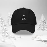 corner cap jnjdjdnbjnddbnksckn black cap with LK embroidery surrounded by paper trees and ornaments.