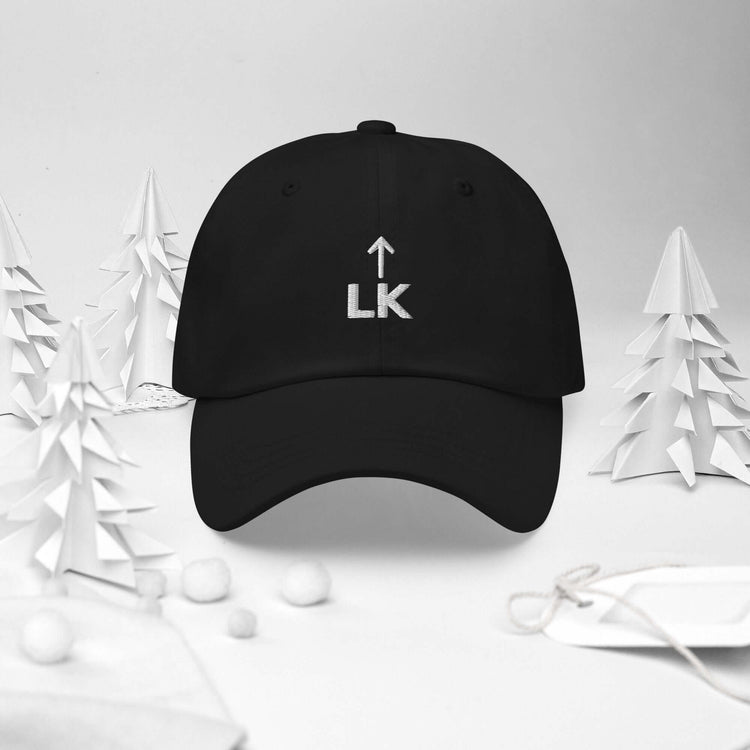 corner cap jnjdjdnbjnddbnksckn black cap with LK embroidery surrounded by paper trees and ornaments.