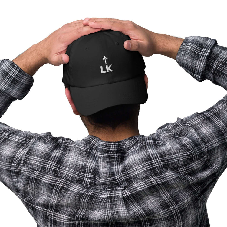 person wearing a black corner cap jnjdjdnbjnddbnksckn, showing embroidered LK and arrow design from the back.